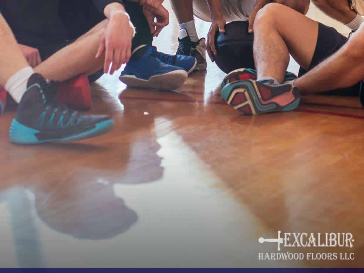 Athletes seated on a court with polished wood, possibly experiencing a squeak gym floor issue during practice