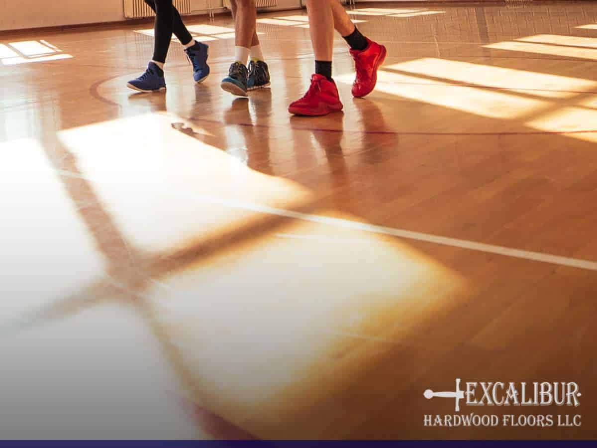 Basketball players running on a polished hardwood floor in a gym.